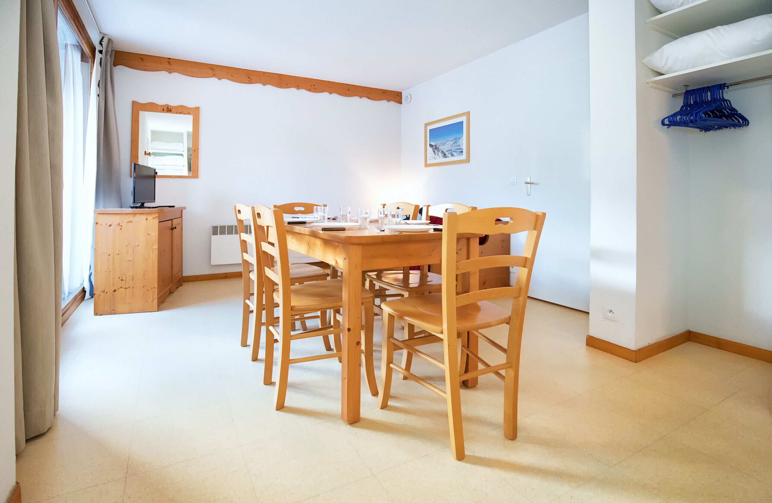 A dining area with a wooden table and chairs, a small cabinet, and a window with curtains.