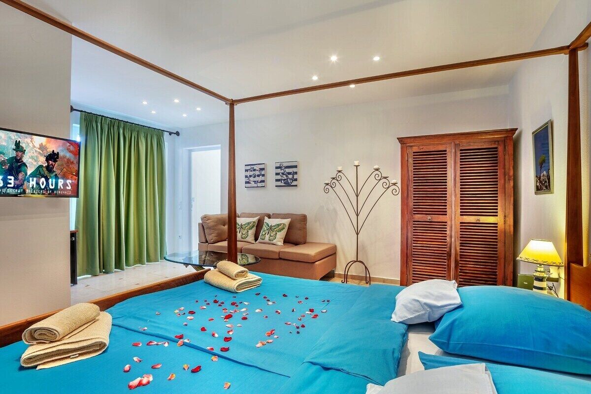 A four-poster bed with blue bedding, a green curtain, a sofa, and a wall-mounted TV.