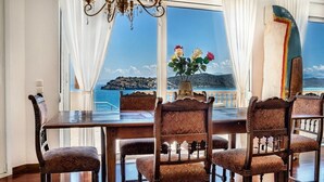 Ein Essbereich mit Tisch und Stühlen, einer Kristallleuchter und Blick auf das Meer durch große Fenster.