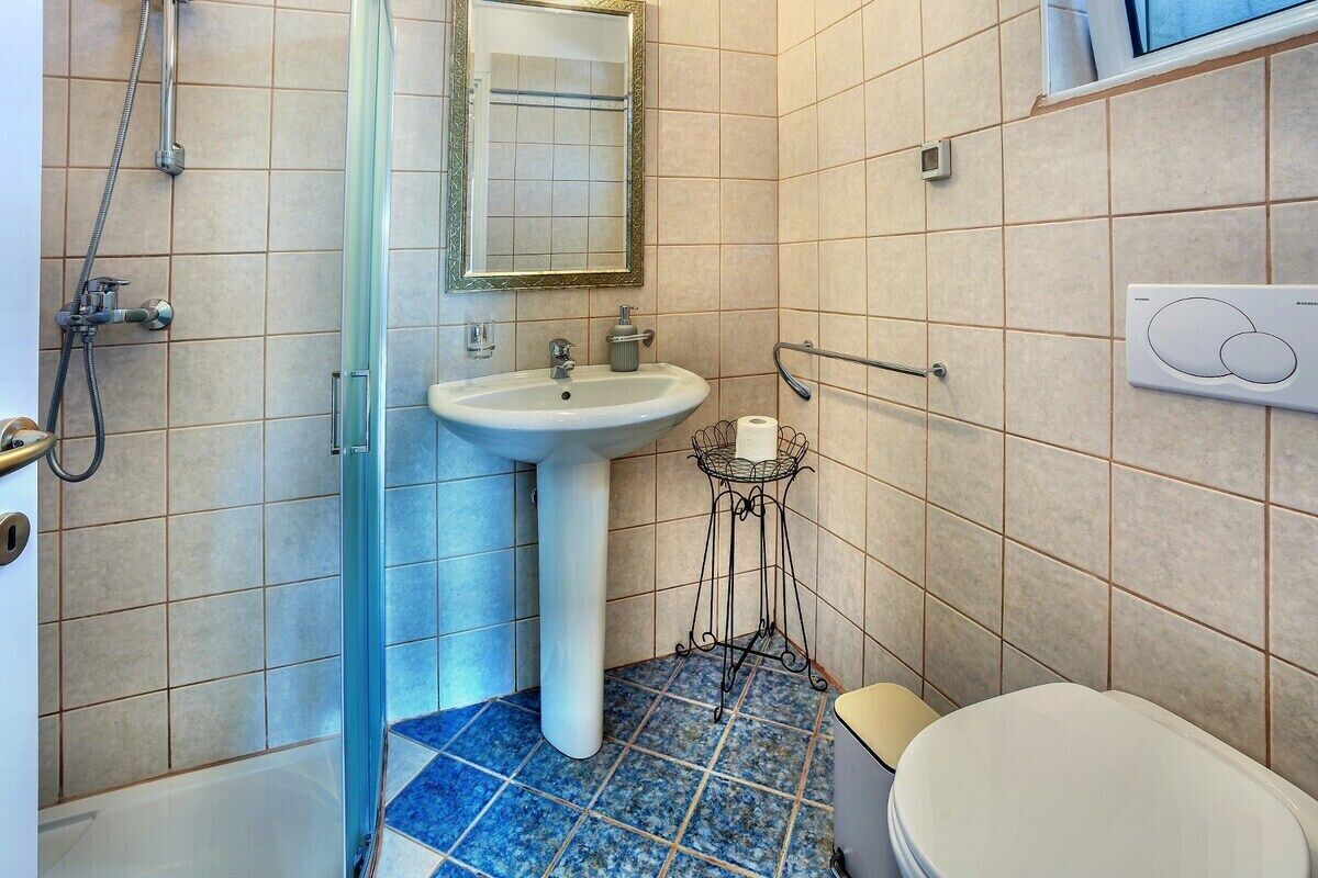 A bathroom with a sink, mirror, shower, toilet, and a towel rack.