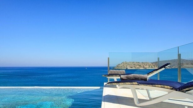 Ein strahlend blauer Himmel, ein Pool mit Meerblick und eine Hügelkulisse im Hintergrund.