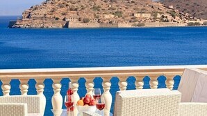 Eine Terrasse mit Korbmöbeln und einem Tisch, der mit Weingläsern und Früchten gedeckt ist, mit Blick auf eine Küstenstadt und das Meer.