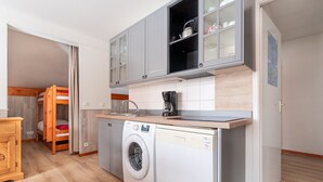 A compact kitchen with a washing machine, wooden cabinets, and a coffee maker.