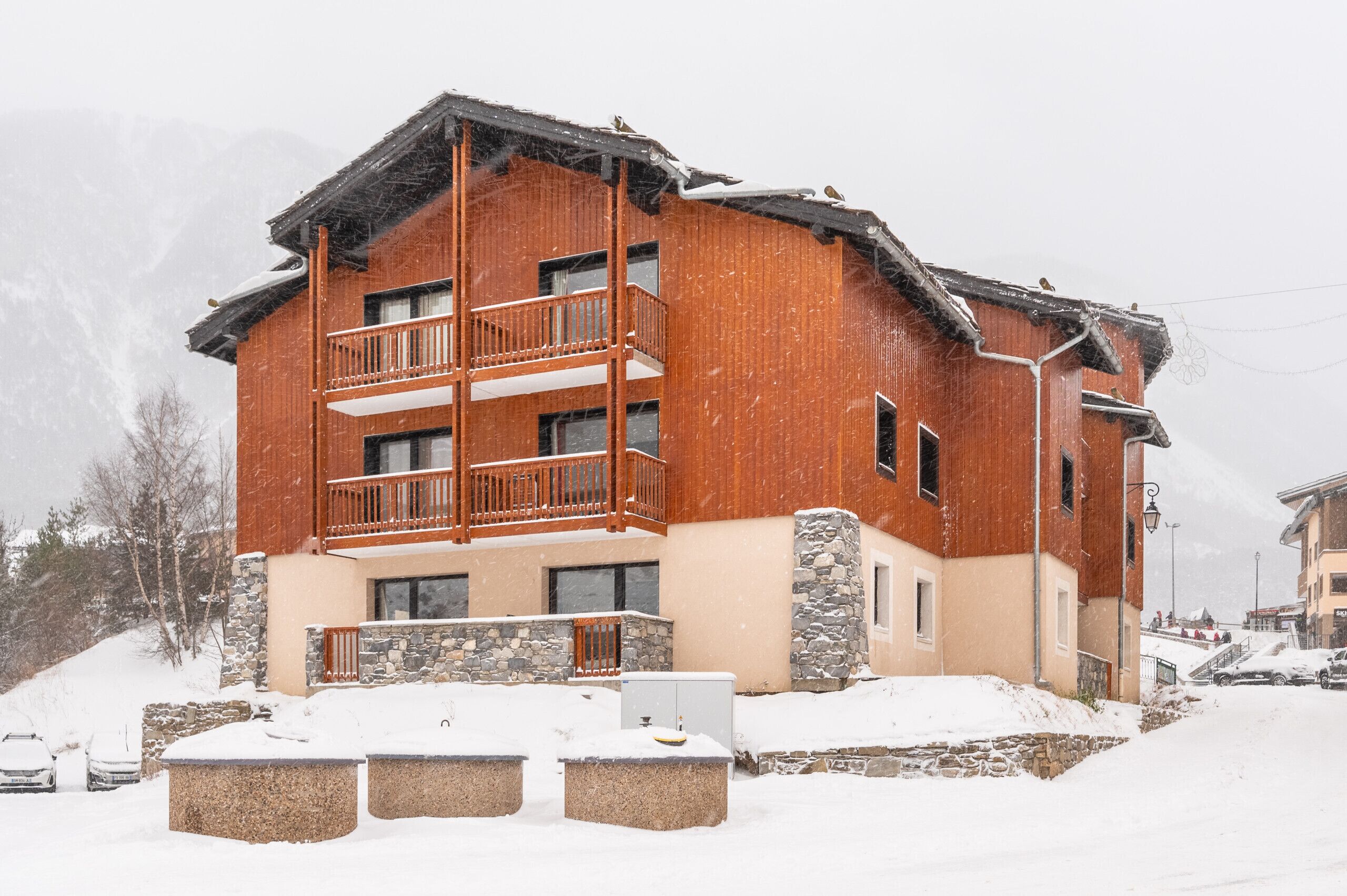 A two-story wooden building with a balcony, stone foundation, and snow-covered surroundings.