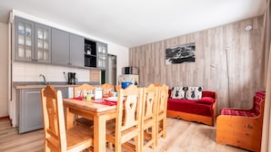A compact living space with a dining area, kitchenette, and a cozy seating area with a red sofa and a small wooden chair.
