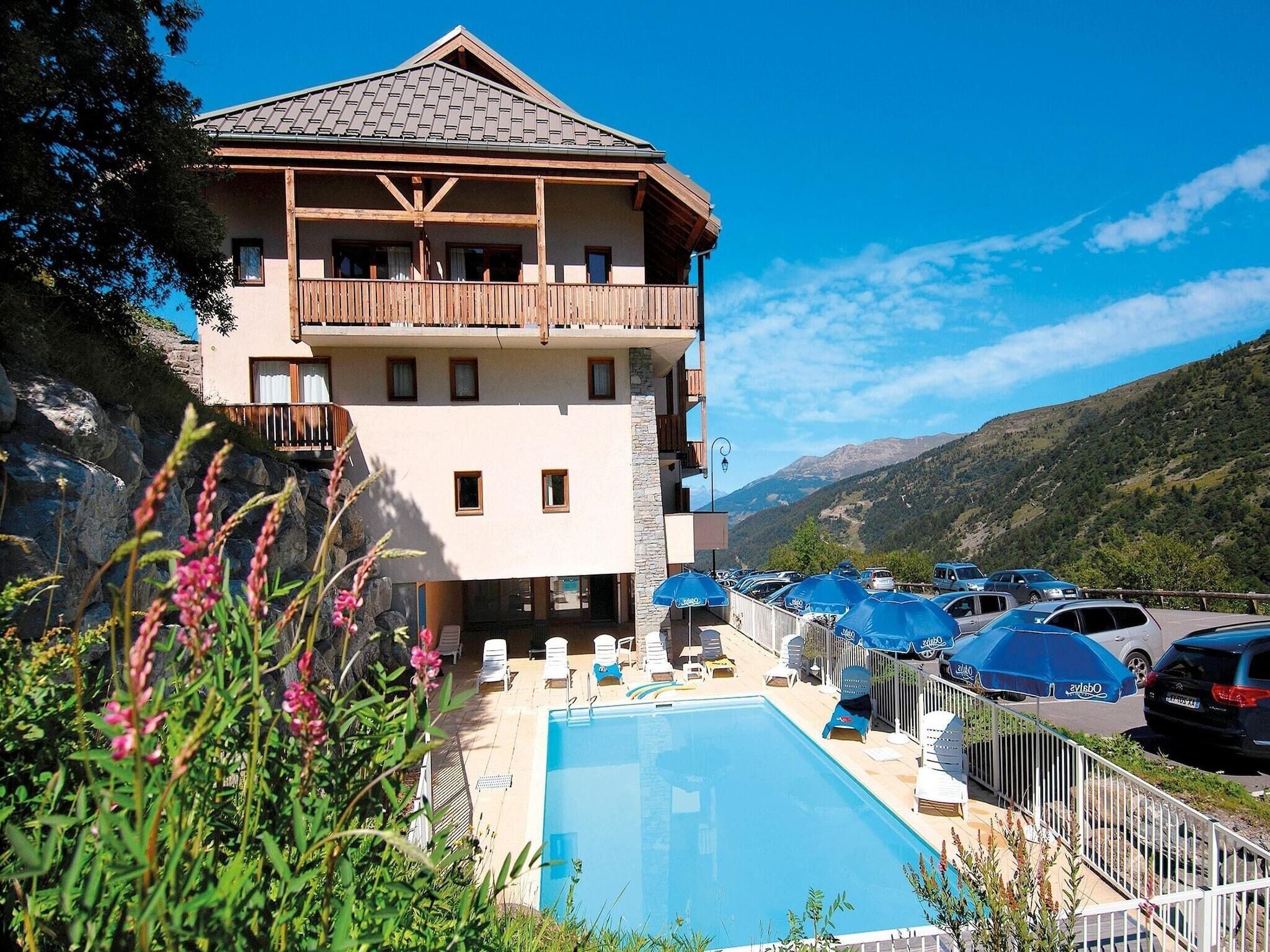 A two-story hotel with a pool, outdoor seating, and a view of the mountains.