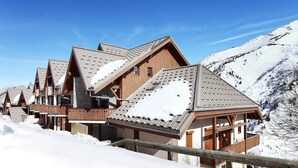 Eine Reihe von Chalets mit steilen Dächern, Holzbalkonen und einem verschneiten Berg im Hintergrund.