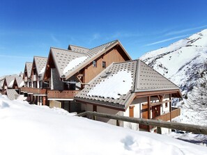 Eine Reihe von Chalets mit steilen Dächern, Holzbalkonen und einem verschneiten Berg im Hintergrund.