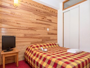 A hotel room with a wooden headboard, a bed with a plaid bedspread, a television on a wooden stand, and a white wardrobe.