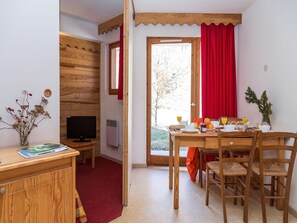 A room with a wooden desk, a television, a dining table with chairs, and a red curtain.
