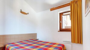 Een slaapkamer met een bed, gordijnen voor het raam, een hoofdeinde en een radiator.