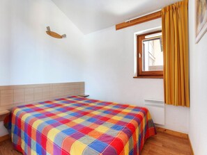 Ein Schlafzimmer mit einem Bett, einem Fenster mit Vorhängen, einem Kopfteil und einer Heizung.