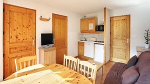 Een compacte keuken met houten kastjes, een magnetron en een klein zite hoekje met een tafel en stoelen.