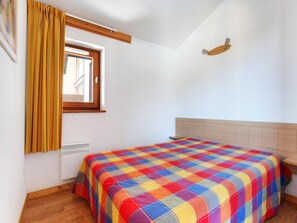 A bedroom with a wooden headboard, a colorful quilt, a window with curtains, and a wall-mounted light fixture.