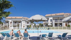 Ein Poolbereich mit Liegestühlen und Sonnenschirmen, umgeben von einem Gebäude mit Balkonen.