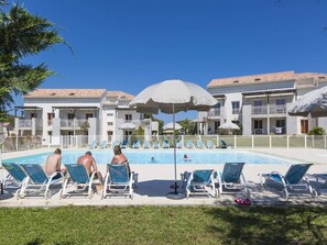 Ein Poolbereich mit Liegestühlen und Sonnenschirmen, umgeben von einem Gebäude mit Balkonen.
