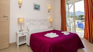Ein Hotelzimmer mit einem Bett, zwei Nachttischlampen, einem Nachttisch, einem Fenster mit Vorhängen und Blick ins Freie.