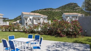 A patio area with a table and chairs, surrounded by greenery and a view of buildings. - Apartment in Corsica near Beaches (Oletta)