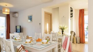 A dining area with a glass table, white chairs, and a television on the wall. - Apartment in Corsica near Beaches (Oletta)