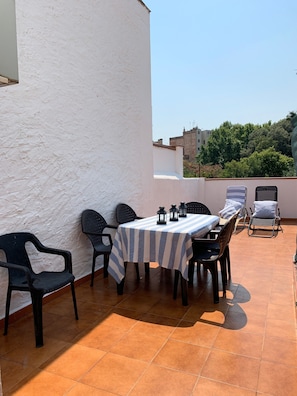 Une terrasse avec une table et des chaises, d’où l’on peut admirer des bâtiments et des arbres en arrière-plan.