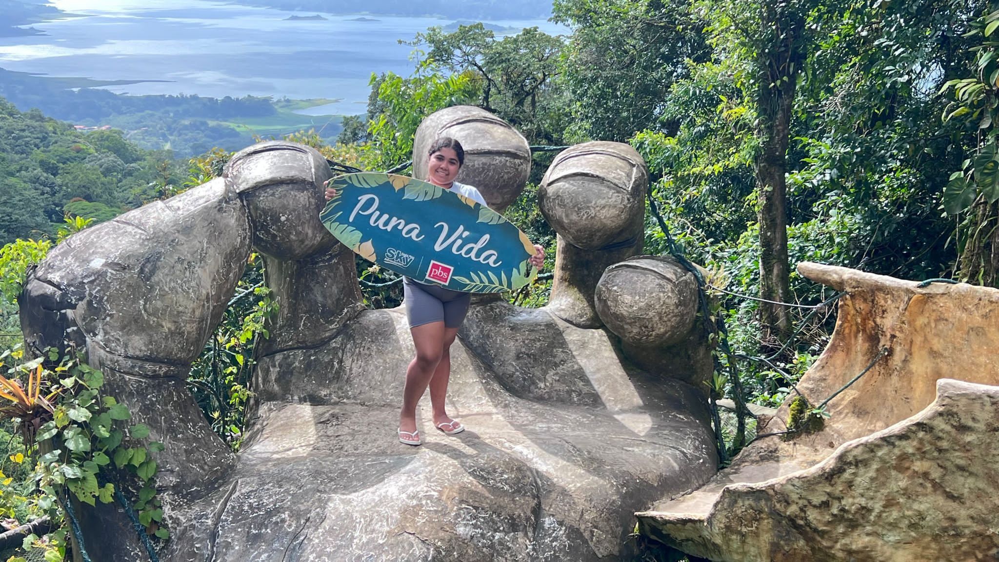 A person standing on a stone structure with a sign that reads "Pura Vida."