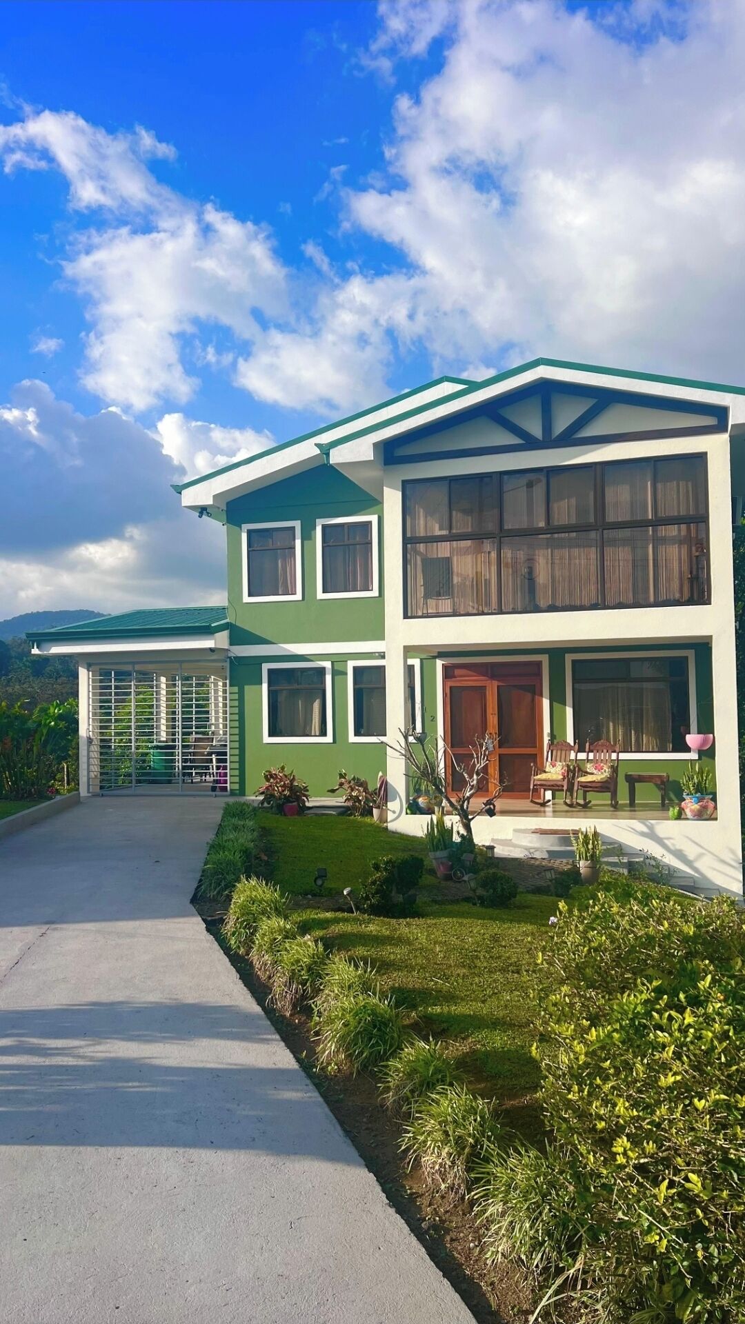A two-story house with a green and white exterior, a covered porch, and a driveway leading to the entrance.