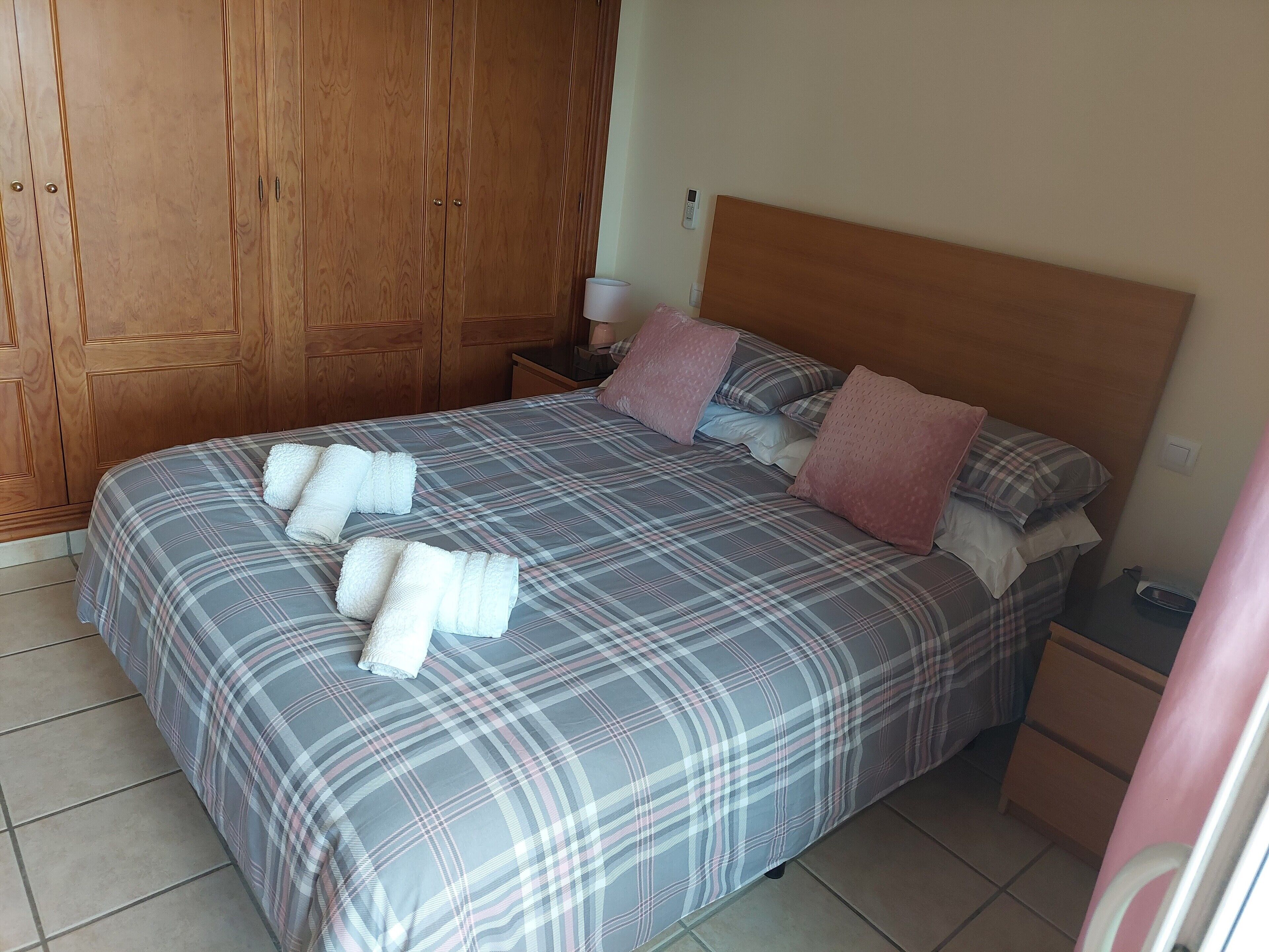 Une chambre à coucher comprenant un lit, une armoire en bois, une table de chevet et une petite table de nuit.