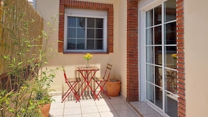 A small patio with a table and chairs, a potted plant, and a window with a view of the outside.