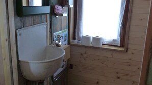 A small, rustic bathroom with a wooden sink, a toilet, and a window with curtains. - La roulotte des Estables (Les Estables)