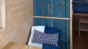 A wooden cabin interior with a bed, a shelf with kitchen items, and a blue door. - La roulotte des Estables (Les Estables)