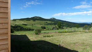 A view from a wooden cabin overlooking a green landscape with a hill and forest. - La roulotte des Estables (Les Estables)