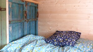 A wooden room with a bed, a blue door, and a wooden ceiling. - La roulotte des Estables (Les Estables)