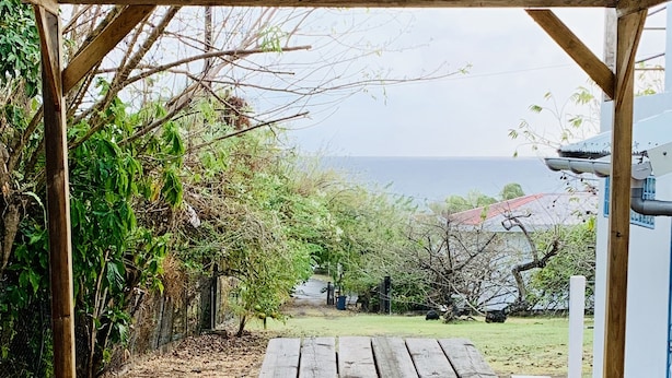 Uma mesa de piquenique de madeira sob uma pérgula de madeira, com vista para o mar.