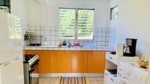 Uma cozinha com armários brancos e laranja, uma pia, uma janela com vista e uma máquina de lavar.