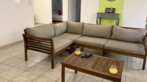 Uma sala de estar com sofá seccional, mesa de centro de madeira e um relógio de parede.