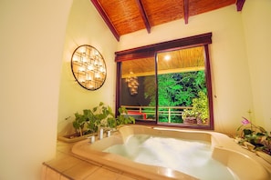 Een badkamer met een groot bad, een raam met uitzicht op groen en een wandlamp.