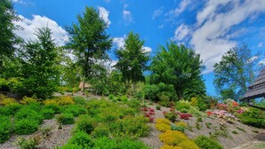 Un jardín con diversas plantas y árboles, un sendero de piedra y un edificio con techo tradicional.
