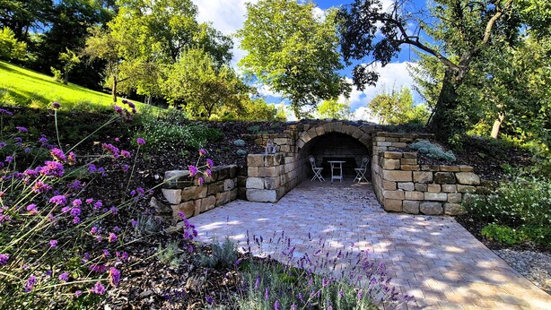 Un arco de piedra que da acceso a un patio con un banco y una mesa de piedra.