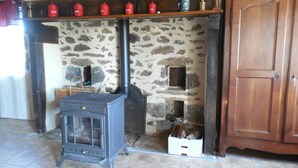 A stone fireplace with a wood-burning stove, a wooden cabinet, and a tiled floor. - $ ATYPICAL COUNTRY HOUSE (Sauvagnat)