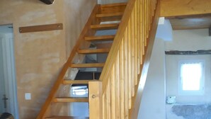 A wooden staircase with a handrail, leading to an upper floor. The floor is tiled, and there is a window on the upper floor. - $ ATYPICAL COUNTRY HOUSE (Sauvagnat)