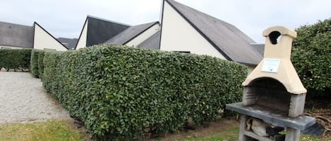 Un jardín con horno de piedra, setos bien cuidados y un sendero de grava.