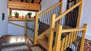 Una scala in legno con corrimano e balaustre nere, che conduce a un pianerottolo con una finestra che si affaccia su un muro in mattoni.
