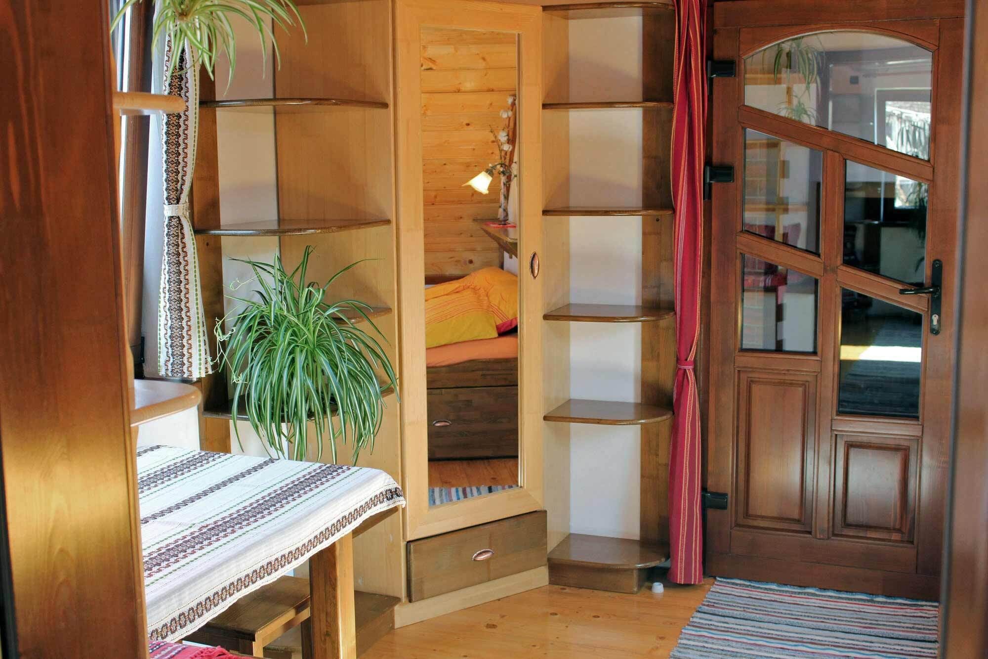 Una habitación acogedora con cama, un armario de madera, una planta y una ventana con cortinas.