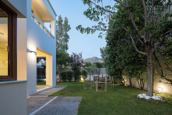 Una casa moderna con césped cuidado, mobiliario de exterior y un árbol.