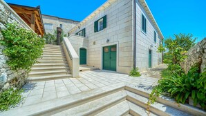 Un edificio de piedra con una escalera que lleva a una puerta verde, rodeado de follaje y un cielo azul despejado.