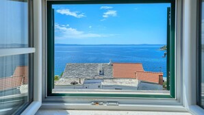 Vista desde una ventana sobre una zona costera con cielo despejado y mar tranquilo.