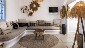 Ein modernes Wohnzimmer mit einem beigen Sofa, gemusterten Kissen, einem gewebten Couchtisch und Wandbildern.