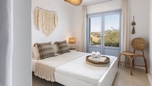 Ein Schlafzimmer mit einem großen Bett, einem Korbsessel, einem Fenster mit Aussicht und einer Pendelleuchte.