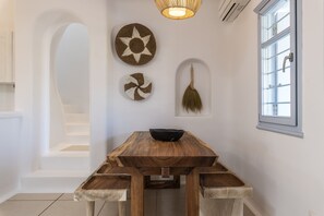 A dining area with a wooden table and chairs, a wall-mounted fan, and a window with a view.