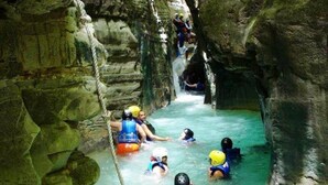 A group of people in a water-filled cave with rocky walls, wearing helmets and life vests.